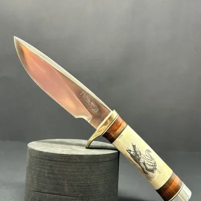 Sale Photo Thumbnail #152: Randall Made fixed-blade knife featuring a polished steel blade, brass crossguard, and an scrimshaw-engraved bone handle depicting an alligator.