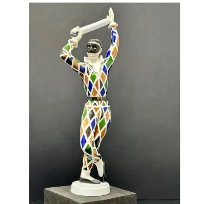 Sale Photo Thumbnail #202: Vintage porcelain Harlequin figurine in a colorful diamond-patterned suit, holding a sword overhead in a striking pose.