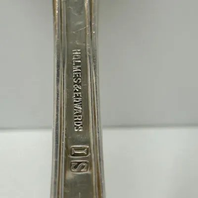 Sale Photo Thumbnail #197: Close-up detail of a silverplate flatware piece showing the Holmes & Edwards IS maker's mark stamped on the handle.