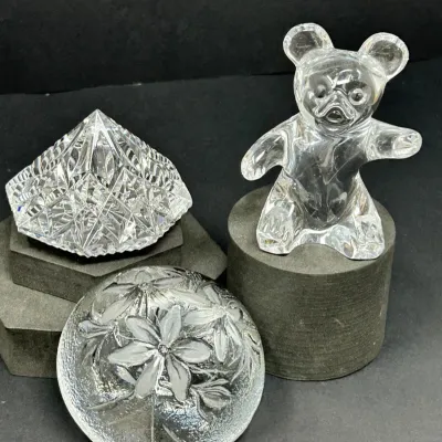 Sale Photo Thumbnail #191: Trio of clear crystal decorative objects, including a standing teddy bear figurine, a diamond-cut pyramid prism paperweight, and a round frosted floral paperweight, all in good condition.