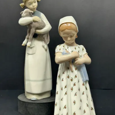 Sale Photo Thumbnail #147: Pair of vintage porcelain figurines depicting young girls, one holding a lamb and the other cradling a doll, both in good condition with soft glazed finishes.