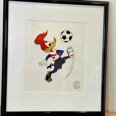 Sale Photo Thumbnail #41: Framed Woody Woodpecker original animation cel featuring Woody playing soccer, complete with an authentication seal and a black frame.