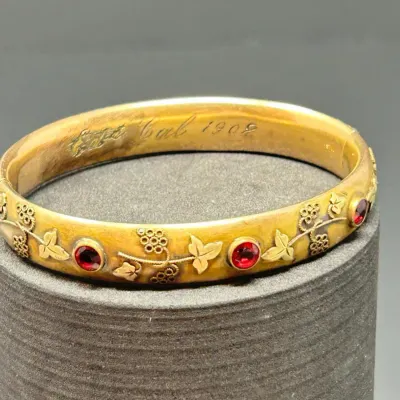 Sale Photo Thumbnail #61: Antique gold-filled bangle bracelet featuring red gemstone accents and a grapevine relief design, inscribed on the interior with the date 1902.