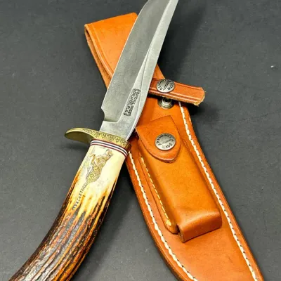 Sale Photo Thumbnail #47: Randall Made fixed-blade knife featuring a stag handle with a scrimshaw leopard detail and brass handguard, accompanied by its original brown leather sheath.