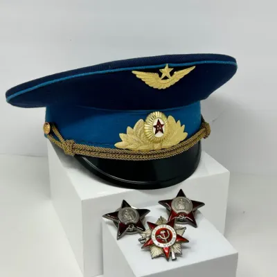Sale Photo Thumbnail #125: Soviet Air Force officer's visor cap featuring insignia and gold-braided chin strap, displayed alongside three Soviet military enamel star medals.