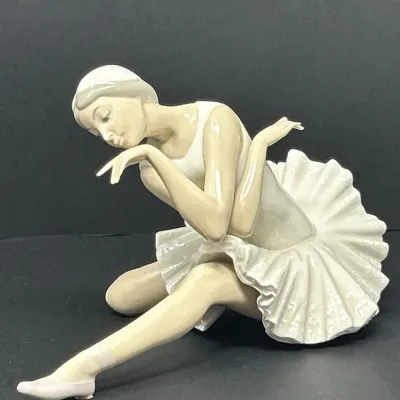Sale Photo Thumbnail #46: Lladro-style glazed porcelain figurine depicting a seated ballerina in a textured tutu, rendered in soft pastel tones.