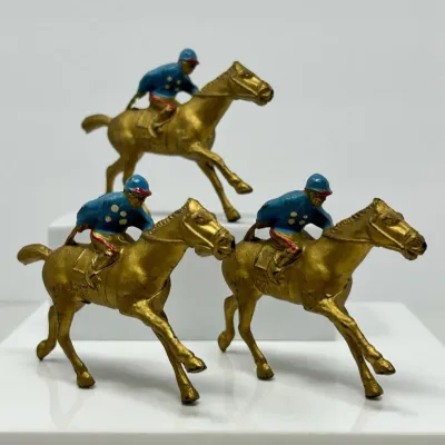 Sale Photo Thumbnail #124: Set of three vintage metal jockey and racehorse figurines, painted in gold tones with blue-clad riders.