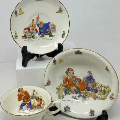 Sale Photo Thumbnail #137: Vintage three-piece porcelain tea set featuring scenes from Gulliver's Travels, including a teacup, saucer, and small bowl with gilt rims.