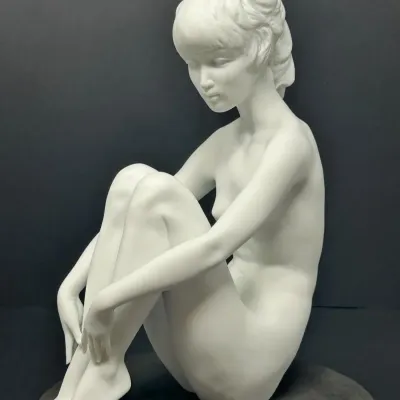 Sale Photo Thumbnail #22: Vintage matte white porcelain figurine depicting a seated nude woman in a contemplative pose, mounted on a dark circular base.