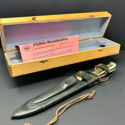 Sale Photo Thumbnail #150: Vintage Puma Waidblatt hunting knife set in green leather sheath, accompanied by original wooden presentation box and paper insert.