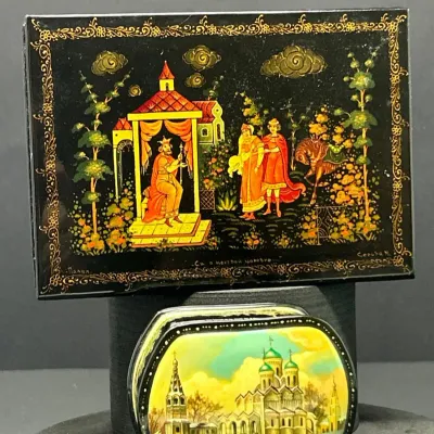 Sale Photo Thumbnail #123: Two Russian Palekh miniature hand-painted lacquer trinket boxes featuring detailed folk tale and architectural scenes with ornate gold borders.