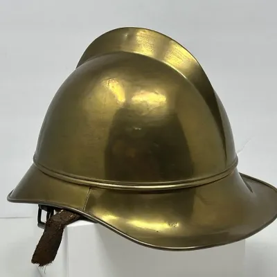 Sale Photo Thumbnail #126: Vintage polish brass firefighter helmet with top comb, flared brim, and leather chin strap.