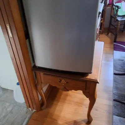Sale Photo Thumbnail #41: Compact Frigidaire mini-refrigerator with a brushed-metal finish, sitting atop a Queen Anne-style wooden end table.