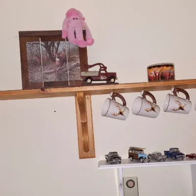 Sale Photo Thumbnail #22: Wall-mounted wooden display shelf featuring rustic decor, including a deer framed picture, small die-cast vehicles, and a set of four suspended deer-themed mugs.