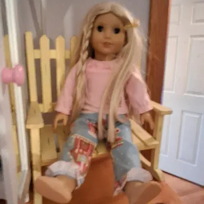 Sale Photo Thumbnail #11: American Girl doll with blonde hair wearing a pink shirt and patterned pants, seated on a small wooden bench.