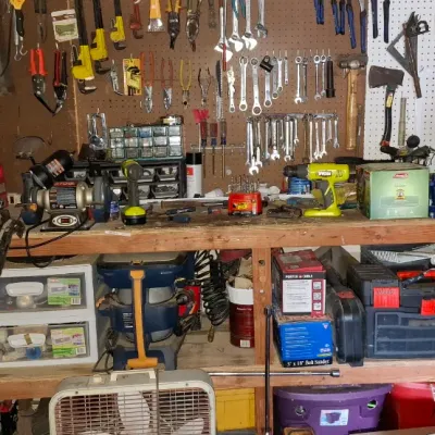 Sale Photo Thumbnail #152: Workshop area filled with various hand tools, power tools, pegboard organizers, and storage bins on and around a wooden workbench.