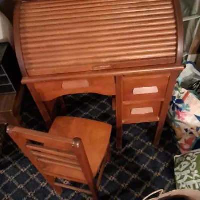 Sale Photo Thumbnail #131: Child-sized wooden roll-top desk with matching ladder-back chair, featuring side drawers and a curved tambour top.