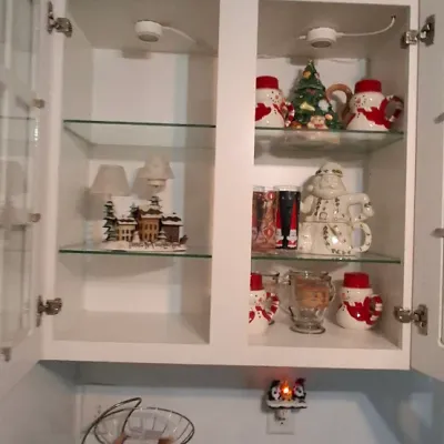 Sale Photo Thumbnail #52: Collection of holiday-themed kitchenware, including snowman and Santa teapots and mugs, arranged inside a white glass-front cabinet.
