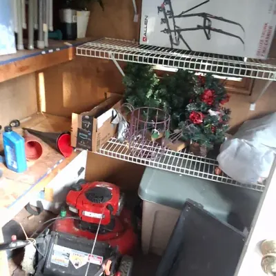 Sale Photo Thumbnail #139: Storage shed area filled with lawn mowers, an Allen Sports bike rack in box, artificial Christmas greenery, and home maintenance tools.