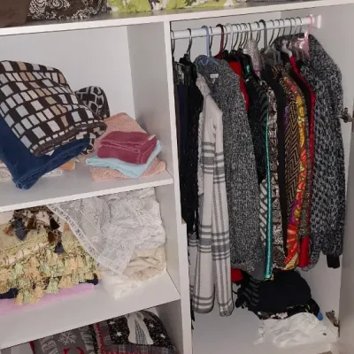 Sale Photo Thumbnail #17: White wooden wardrobe unit filled with folded linens, blankets, decorative pillows, and hanging women's clothing.