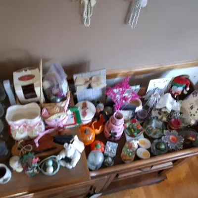 Sale Photo Thumbnail #45: Collection of home decor items, holiday knick-knacks, taper candles, and small tabletop figurines displayed on a wooden cabinet.