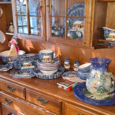 Sale Photo Thumbnail #28: Large wooden china hutch filled with a collection of blue winter and cabin motif dishware, including mugs, plates, bowls, and a pitcher.