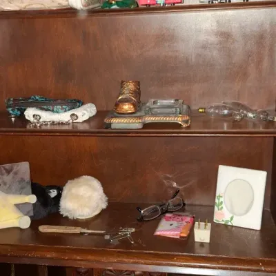Sale Photo Thumbnail #72: Wooden shelving unit filled with various household items, including holiday snow globes, linens, novel stacks, decorative accents, and picture frames.