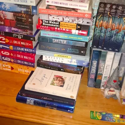 Sale Photo Thumbnail #66: Large assortment of contemporary paperback and hardcover fiction books stacked on a wooden dresser.