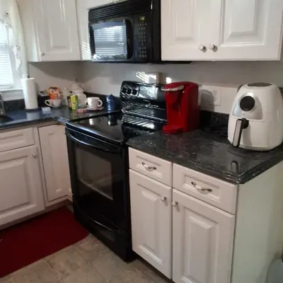 Sale Photo Thumbnail #47: Kitchen space featuring white cabinetry, dark stone countertops, a black electric range and microwave, a red Keurig coffee maker, and a white air fryer.