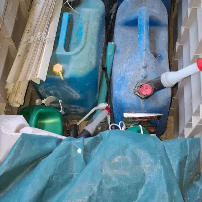 Sale Photo Thumbnail #155: Collection of outdoor and lawn care items stored in a plastic bin, including blue kerosene jugs, a green plastic watering can, and window blinds.