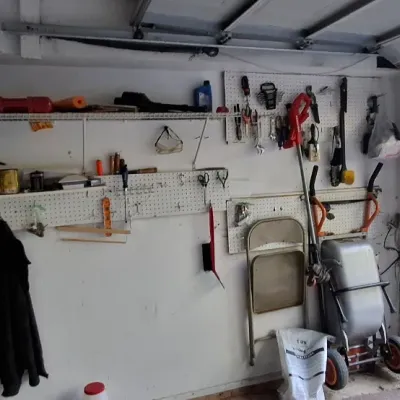 Sale Photo Thumbnail #158: Organized garage workshop featuring pegboard tool storage, wall-mounted wire shelving, hand tools, and a two-wheeled utility dolly.