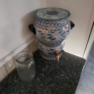Sale Photo Thumbnail #48: QVC Blue and white patterned ceramic water dispenser crock with lid, black side handles, and spigot, shown alongside a clear glass jar.