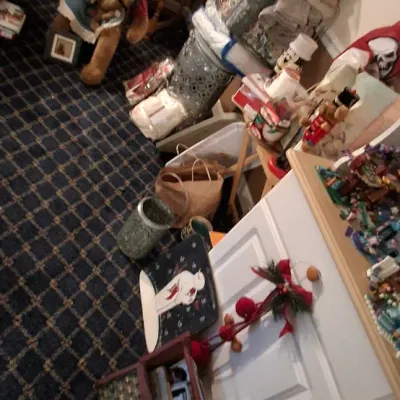 Sale Photo Thumbnail #122: Collection of holiday decor and plush teddy bears, including snowmen figures, Christmas ornaments, and folded linens, set up in a carpeted room.