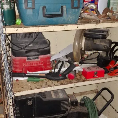 Sale Photo Thumbnail #149: Assorted power tools and workshop items on metal shelving, including a portable air compressor, a Craftsman wet/dry vacuum, and various hard tool cases.