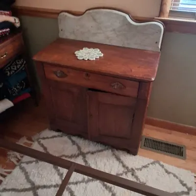 Sale Photo Thumbnail #80: Antique wooden washstand with a marble splashback and lower cabinet doors, displayed on a cream and grey diamond patterned rug.
