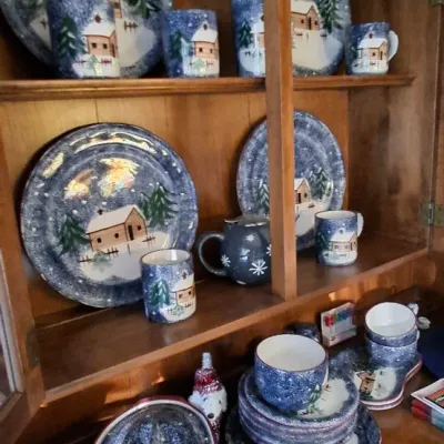 Sale Photo Thumbnail #29: Collection of winter cabin themed ceramic dinnerware, including plates, mugs, a covered casserole dish, and serving trays displayed in a wooden hutch.