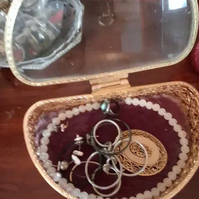 Sale Photo Thumbnail #87: Vintage gold-toned filigree jewelry box with a glass lid, containing various rings, a beaded necklace, and a broach.