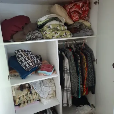 Sale Photo Thumbnail #16: White wooden wardrobe filled with assorted linens, blankets, and hung clothing.