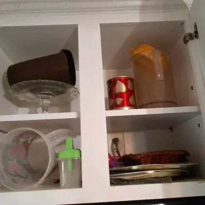 Sale Photo Thumbnail #53: Open white kitchen cabinet containing vintage plastic pitchers, a clear glass cake stand, a decorated tin, and various serving items.