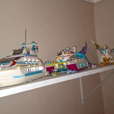 Sale Photo Thumbnail #132: Collection of assembled Lego Friends and Elves building sets displayed on a shelf, including a cruise ship, catamaran, and dragon.