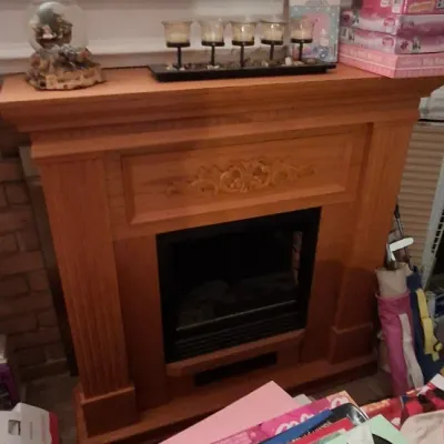 Sale Photo Thumbnail #116: Freestanding electric fireplace with a light oak wooden mantel surround, topped with decorative tabletop accents and candle holders.