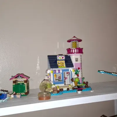 Sale Photo Thumbnail #129: Collection of assembled LEGO Friends playsets lined up on a shelf, including a lighthouse, jungle treehouse, airplane, and yacht.