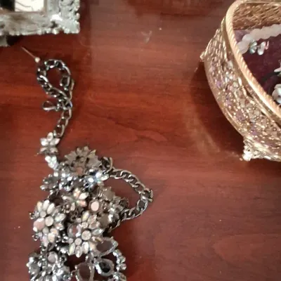 Sale Photo Thumbnail #86: Statement necklace featuring dark metal curb chain and intricate rhinestone floral motifs, shown alongside an ornate gold-tone jewelry box and framed mirror.