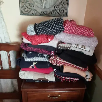 Sale Photo Thumbnail #82: Large stack of patterned knit sweaters piled high on a traditional wooden single-drawer nightstand, topped by a metal scrollwork floral wall art panel.