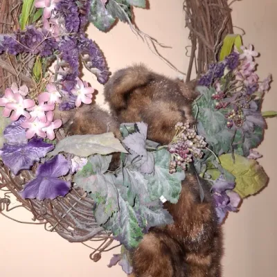 Sale Photo Thumbnail #71: Grapevine floral wreath featuring artificial purple and pink flowers, greenery, and a plush teddy bear nestled in the center.