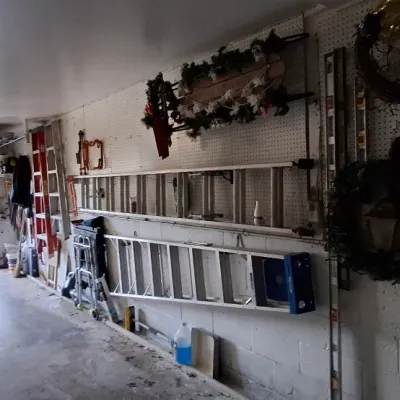 Sale Photo Thumbnail #157: Garage storage area featuring several aluminum extension and step ladders mounted on pegboard walls, alongside holiday wreaths and decor.