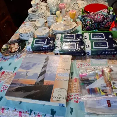 Sale Photo Thumbnail #32: Dining table filled with household items including stacks of china, a Heritage lighthouse jigsaw puzzle, packages of adult wipes, and art supplies.