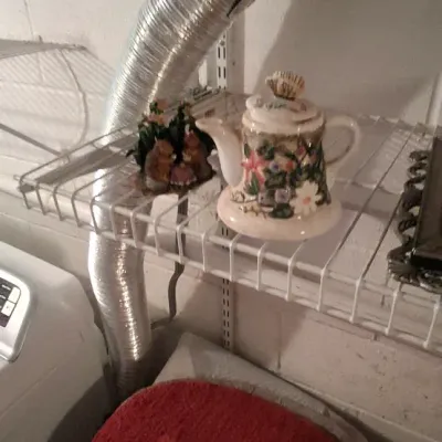 Sale Photo Thumbnail #108: Small ceramic decorative teapot with floral relief and shell finial displayed on a white wire utility shelf.