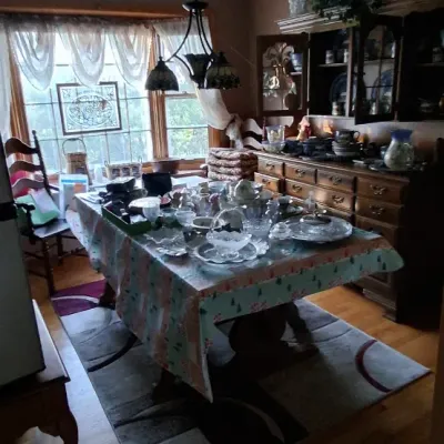 Sale Photo Thumbnail #60: Dining room featuring a wooden TRESTLE table set with glassware, an overhead three-light chandelier, a area rug, and a large traditional wooden hutch in the background.