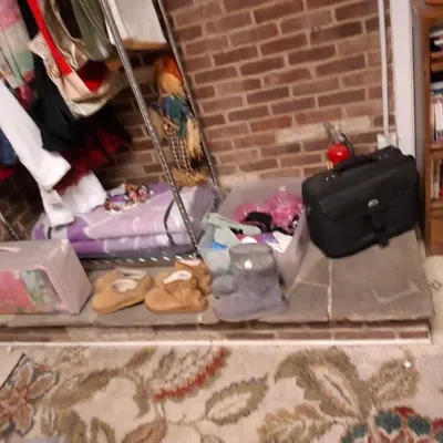 Sale Photo Thumbnail #63: Indoor area featuring a clothing rack with various garments, footwear on the hearth, a black briefcase, and a wooden bookcase filled with books.